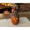 This is a carved pumpkin gourd named Carsen. He has a happy face carved into the shell and his top is decorated with real pine cone scales.